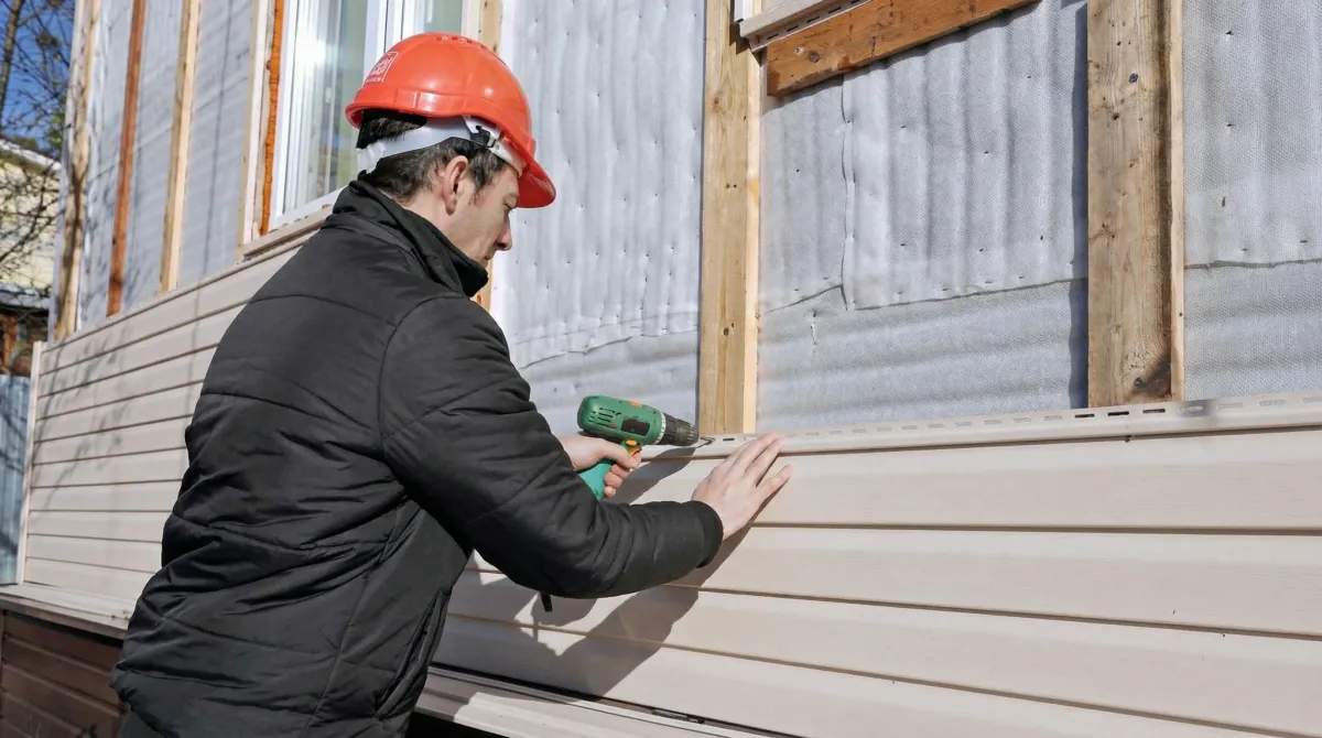Siding replacement professional using a power drill to install new tan vinyl siding on a home exterior in Ogden, UT